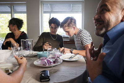 Friends using phone while family talking at dining table in dinner party