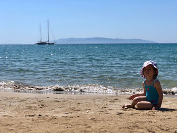 Girl sitting on shore at beach against sky
