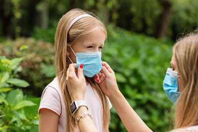 Mother putting mask on daughters face at park