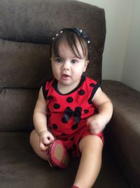 Portrait of cute baby girl sitting on sofa at home