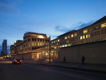 Cars on road by illuminated buildings against sky at dusk