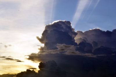 Low angle view of sunlight streaming through clouds during sunset