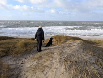 Woman walking with dog on beach against sky