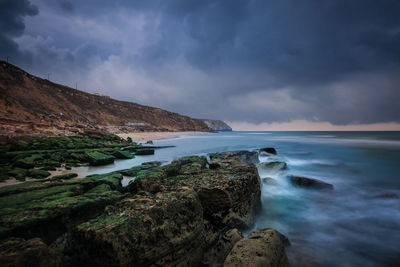 Scenic view of rock formations by sea against cloudy sky