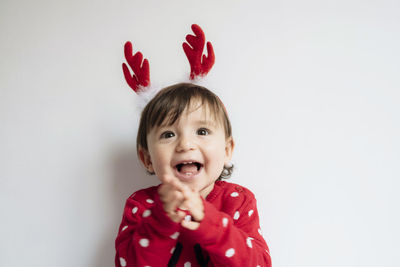 Portrait of happy baby girl with reindeer antlers headband singing and clapping hands