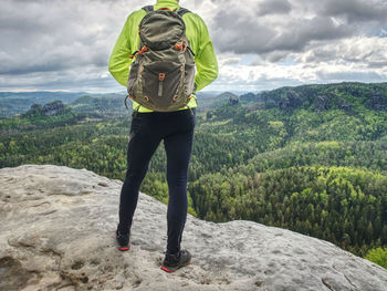 Climber man with backpack and trekking clothes on the top of a hill, agains mountains.