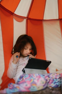 Four-year-old girl in pajamas looking at tablet in a little house