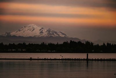 Scenic view of lake by snowcapped mountains against sky during sunset