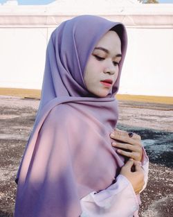 Young woman wearing hijab looking down against wall