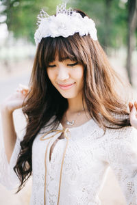 Close-up of beautiful young woman wearing white dress and wreath in forest