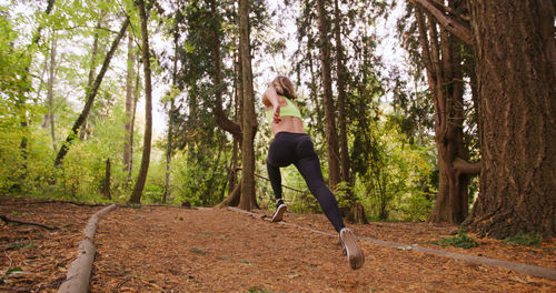 Rear view of woman running by trees in forest