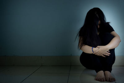 Woman sitting on tiled floor against wall at home