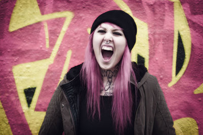 Beautiful woman with dyed hair shouting against graffiti wall