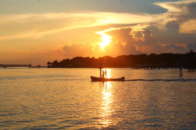 Silhouette people in boat at sea against sky during sunset