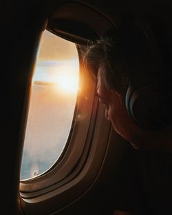 Man looking through airplane window during sunset