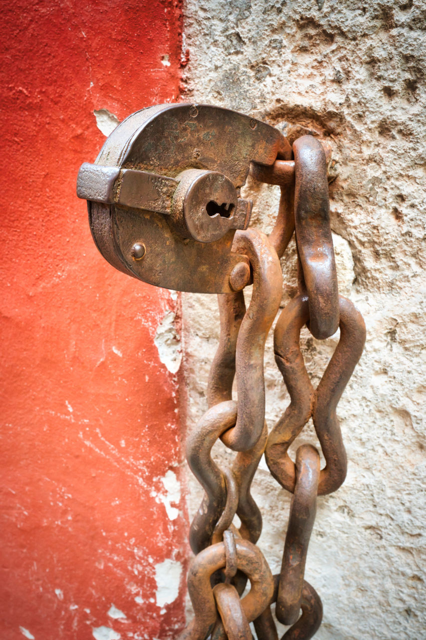 CLOSE-UP OF RUSTY METAL CHAIN AGAINST RED WALL