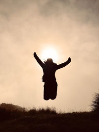 Woman silhouette jumping with arms outstretched against sky during sunrise reaching  mountain top