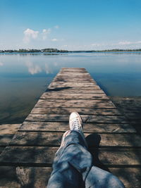 Low section of man lying on jetty in lake against sky