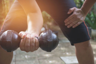 Midsection of man lifting dumbbell while standing outdoors