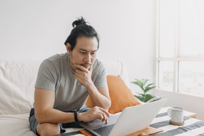 Young man using mobile phone while sitting on bed at home