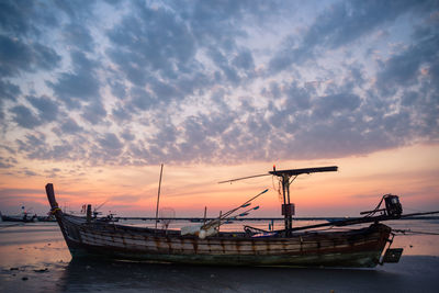 Boat moored on beach against sky during sunset