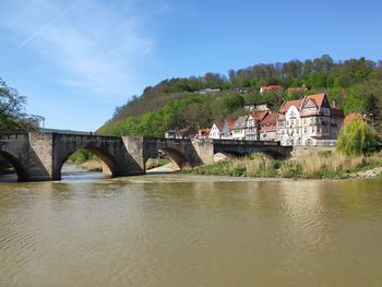 Arch bridge over river by building against sky