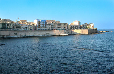 Buildings by sea against clear blue sky