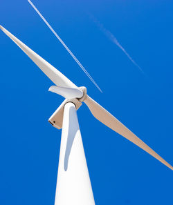 Wind turbine against a blue sky with a jet airplane passing overhead