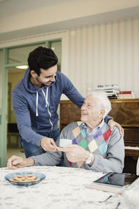 Caretaker serving coffee to senior male in living room at home