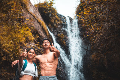 Young couple enjoying the beautiful waterfall view and showing thumbs up in the camera.