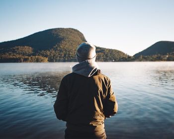 Rear view of woman standing by lake against clear sky