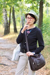 Portrait of woman smoking cigarette while standing at forest