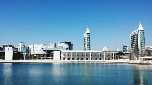 Modern buildings by swimming pool against clear blue sky