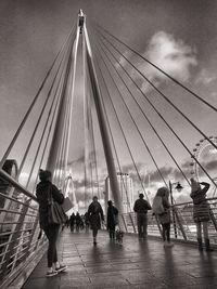 People on suspension bridge against sky