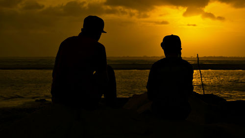 Rear view of silhouette people overlooking calm sea