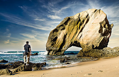 Man standing on rock by sea against sky