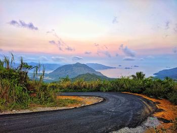 Road by mountains against sky during sunset