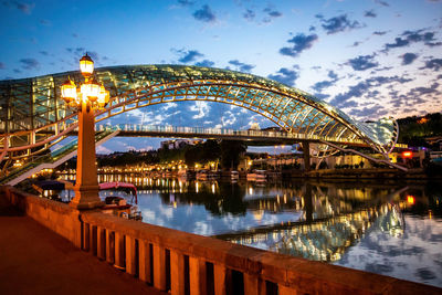 Illuminated bridge over river against sky in city