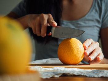 Midsection of woman cutting orange on board