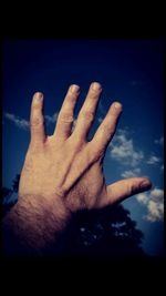 Close-up of hands against blue sky