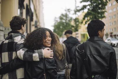 Boy with arm around female friend looking over shoulder while walking at street