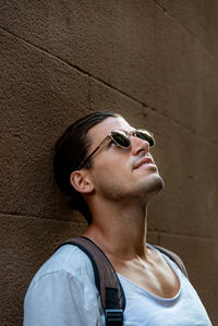 Portrait of young man wearing sunglasses standing against wall