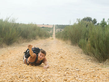 Portrait of young man lying on dirt road against sky