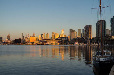 River by illuminated city against clear sky during sunset