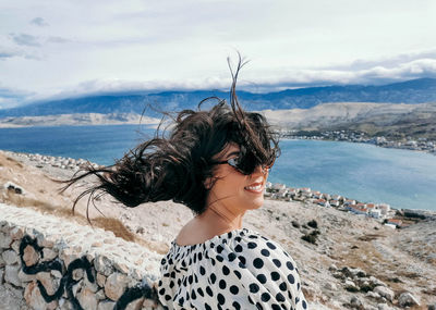 Rear view of young woman on viewpoint over sea. wind blowing hair.