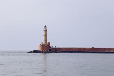 Lighthouse by sea against clear sky