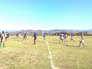 People playing football on field against clear blue sky