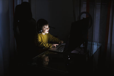 Boy wearing headphones using laptop on table at home