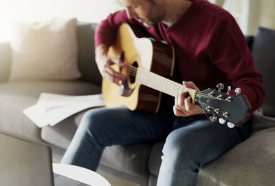 Midsection of man playing guitar at home