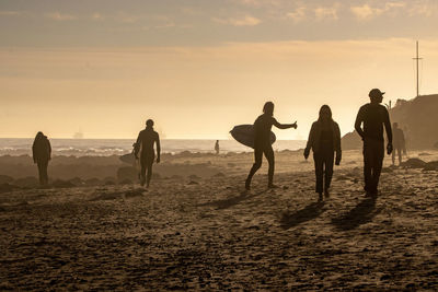 Silhouette people on beach against sky during sunset